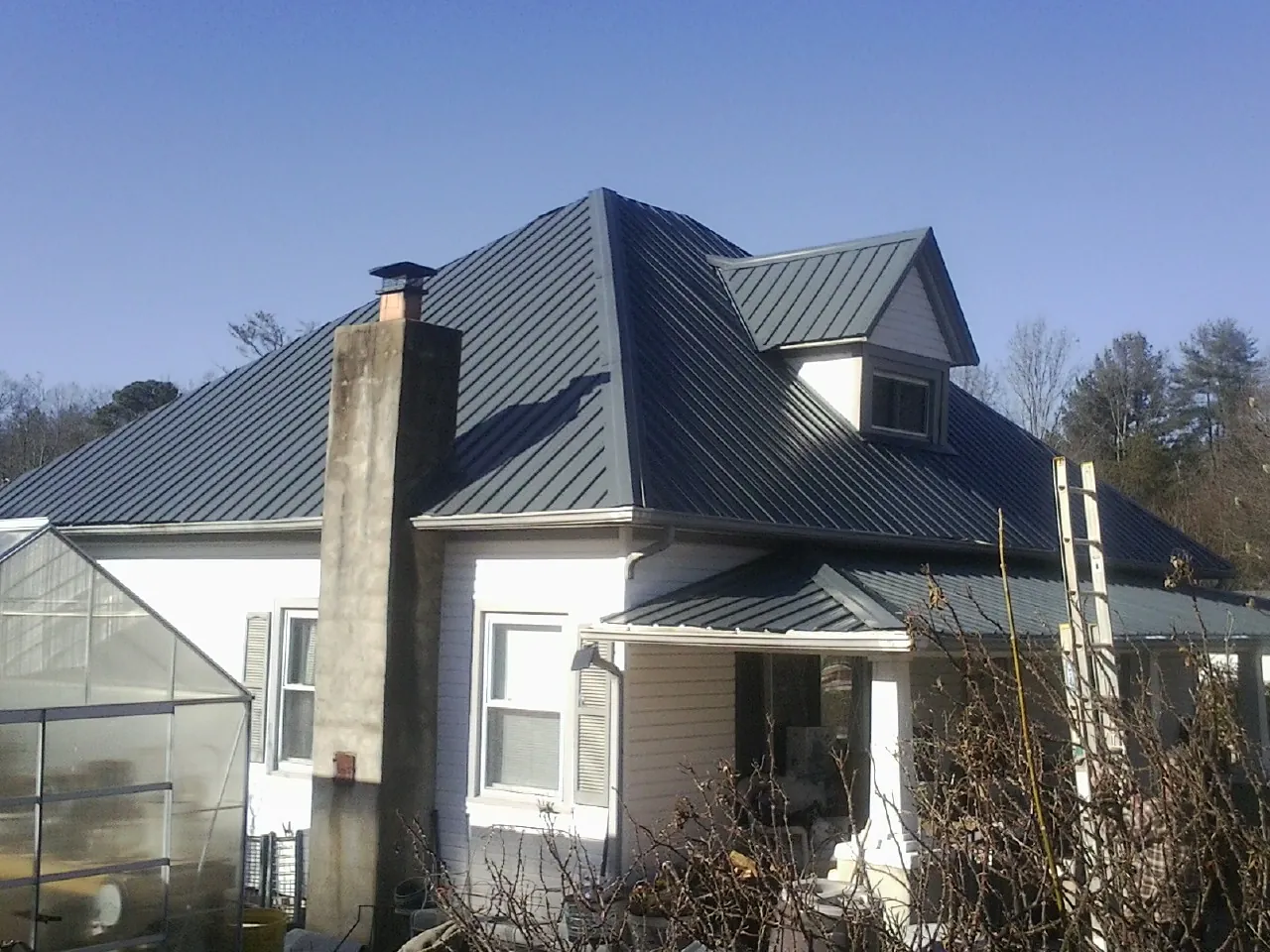 Dark blue standing seam metal roof on a white farmhouse with dormer — Slate & Tile Roof Repair by Roofing Brothers in Lester