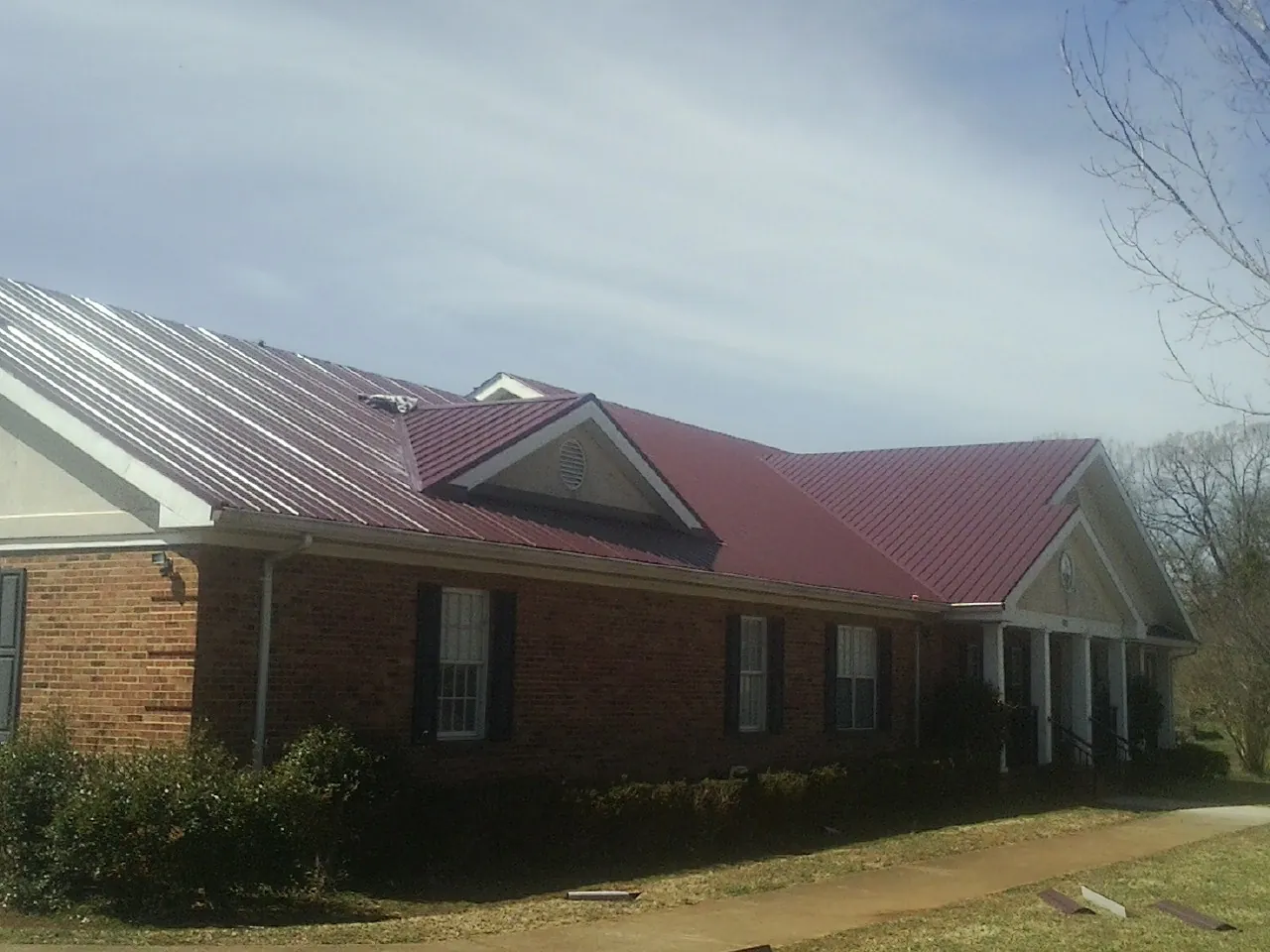 Red metal roof with gabled entries on a long brick building, from a Hail Damage Roof Repair job in Lester