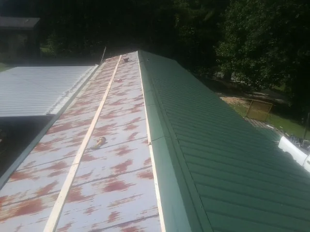 Old rusted panels beside newly installed green metal roofing — Wind Damage Roof Repair by Roofing Brothers in Lester