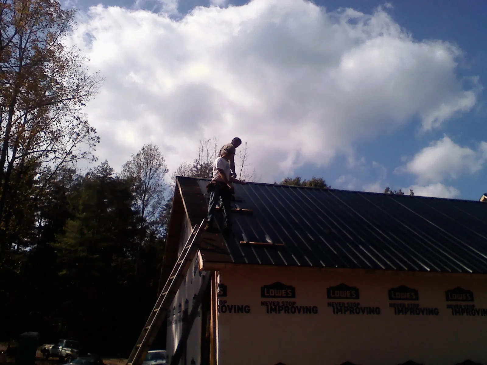 Roofer fastening dark metal panels high against a cloudy sky, from a Roof Inspection job in Lester