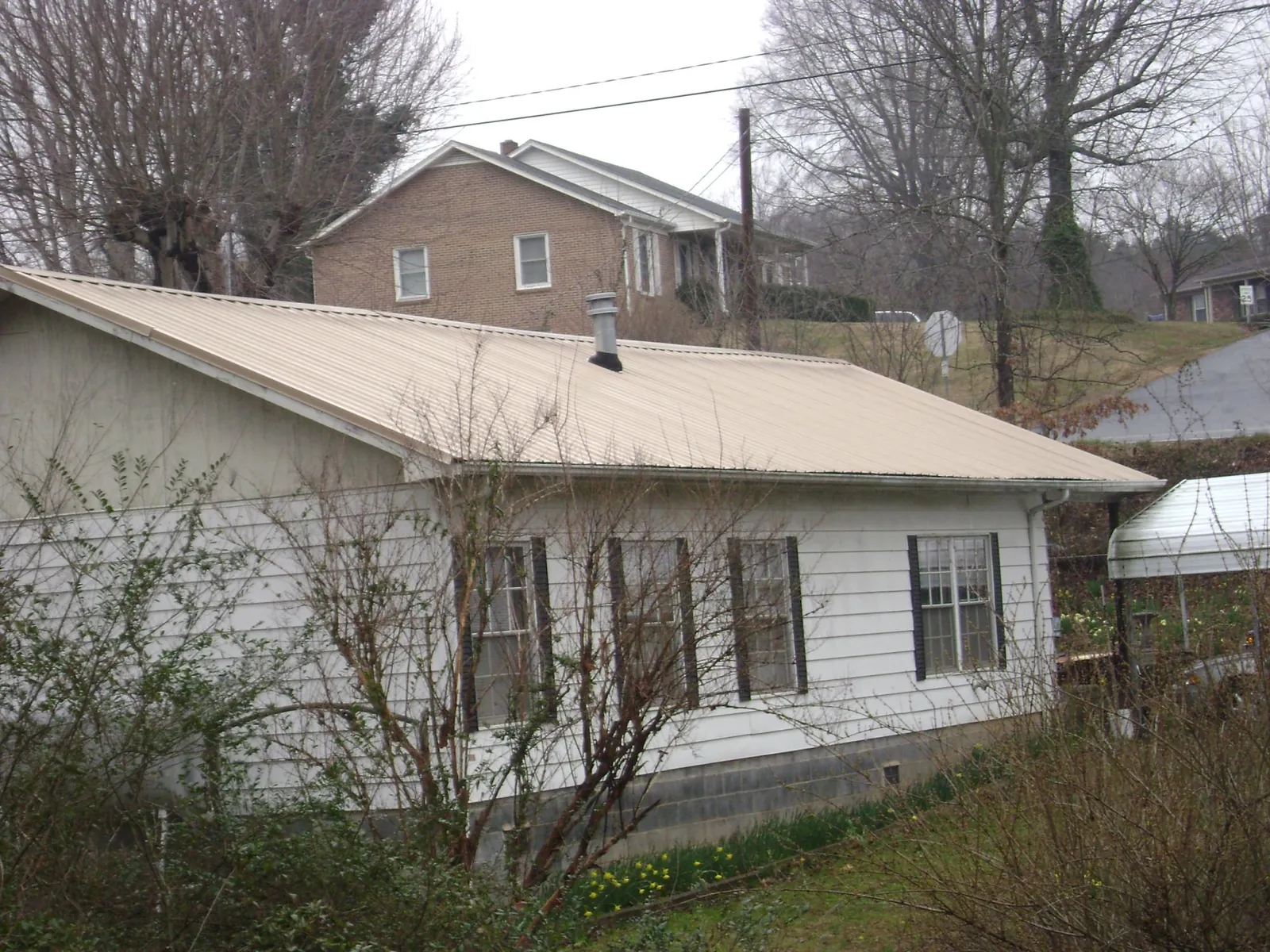 Tan metal roof on a white sided house set into a hillside — Commercial Roofing by Roofing Brothers in Lester