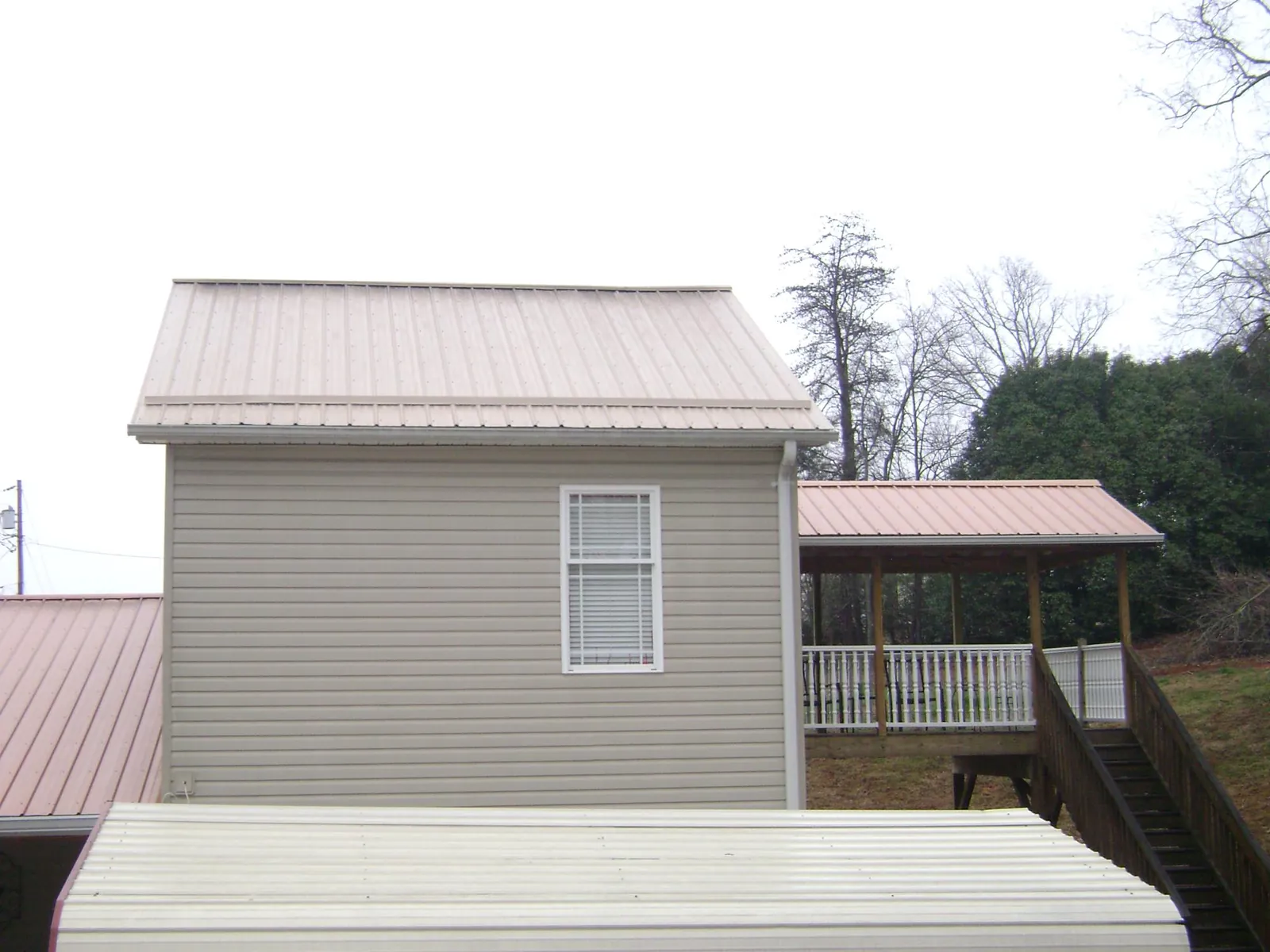 Tan metal roofs on a two story addition and attached porch, from a Roof Replacement job in Lester